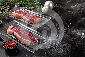 New York beef marbled meat vacuum packed steak in Christmas style, on black dark stone table background, with copy space for text