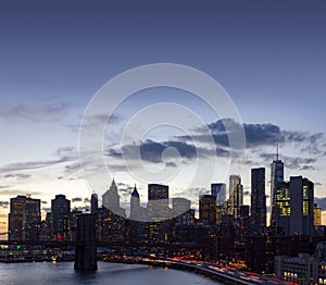 New York City skyline lights at dusk with the Brooklyn Bridge