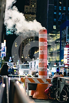 New York, New York - November 16, 2018 : Vapor riding from a manhole in Manhattan through white and orange steam chimneys