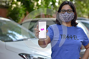 New York, USA, 2020. Girl wearing mask showing Lyft app on her mobile phone screen while standing in front of her fleet of cars.