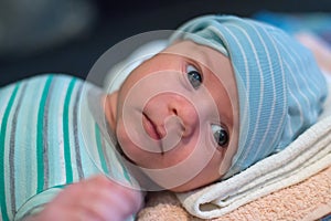The newborn 2 months baby with a hat is lying on the bed and laughing