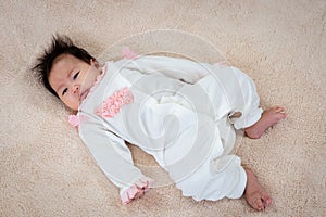 A newborn Asian girl lies in a white dress on the bed waiting for her mother to take care of her. The little boy rolled around on