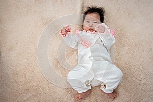 A newborn Asian girl lies in a white dress on the bed waiting for her mother to take care of her. The little boy rolled around on