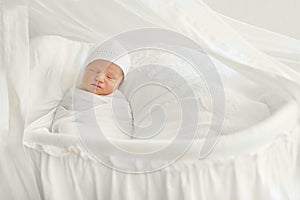 Newborn baby 7 days wrapped in white diaper and hat and sleeping
