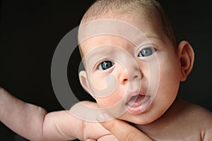 Newborn baby against black background with big eyes looking into the camera being held by her mother