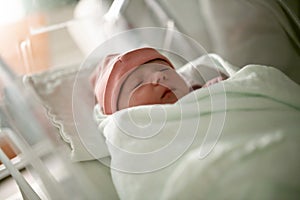 Newborn baby asleep, swaddled in hospital blanket and wearing a hat