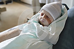 Newborn baby asleep, swaddled in hospital blanket and wearing a hat