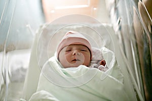 Newborn baby asleep, swaddled in hospital blanket and wearing a hat
