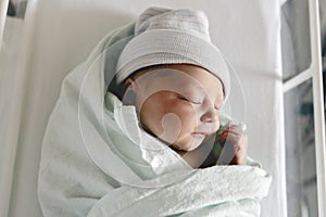 Newborn baby asleep, swaddled in hospital blanket and wearing a hat