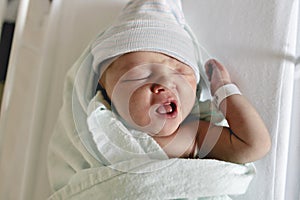 Newborn baby asleep, swaddled in hospital blanket and wearing a hat