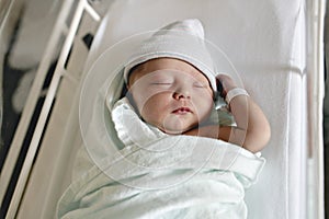 Newborn baby asleep, swaddled in hospital blanket and wearing a hat