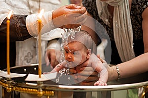 Newborn baby baptism in Holy water. baby holding mother`s hands. Infant bathe in water. Baptism in the font