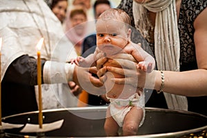 Newborn baby baptism in Holy water. baby holding mother`s hands. Infant bathe in water. Baptism in the font