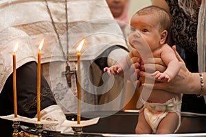 Newborn baby baptism in Holy water. baby holding mother`s hands. Infant bathe in water. Baptism in the font