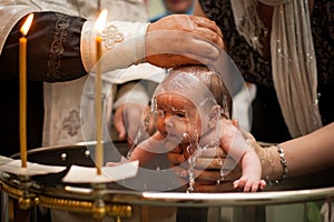Newborn baby baptism in Holy water. baby holding mother`s hands. Infant bathe in water. Baptism in the font
