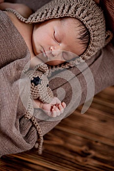 Newborn baby, beautiful infant lies and holding a tiny teddy bear in the bed on wooden background