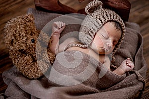 Newborn baby, beautiful infant lies and holding a tiny teddy bear in the bed on wooden background