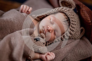 Newborn baby, beautiful infant lies and holding a tiny teddy bear in the bed on wooden background