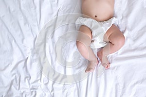 Newborn baby belly and legs in diaper, lying on white bed, top view, copy space