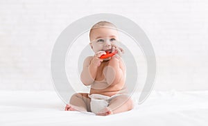 Newborn baby biting red teether in bed