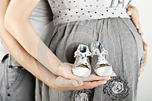 Newborn baby booties in parents hands, Pregnant woman belly