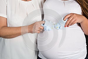 Newborn baby booties in parents hands. Pregnant woman belly.