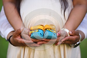 Newborn baby booties in parents hands, Pregnant woman belly. Maternity concept