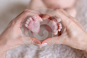 Newborn or Baby born. New Mom or mother doing Heart with fingers. Child or kid feet in mother hand. Barefoot baby.