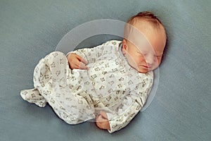 Newborn baby boy asleep on a blue background in white pajamas wi