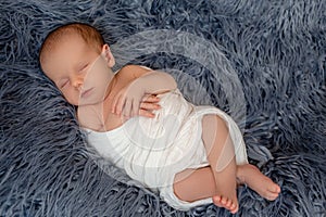 Newborn baby boy in bed. New born child sleeping under a white knitted blanket. Children sleep.