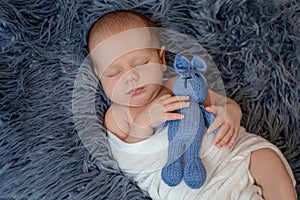 Newborn baby boy in bed. New born child sleeping under a white knitted blanket. Children sleep.