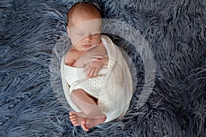 Newborn baby boy in bed. New born child sleeping under a white knitted blanket. Children sleep.