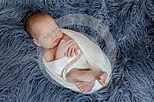 Newborn baby boy in bed. New born child sleeping under a white knitted blanket. Children sleep.