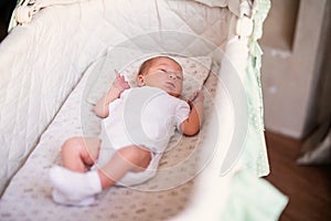 Newborn baby boy in bed. New born child in white bodykit lying in light cradle. Children sleep. Bedding for kids. Infant napping