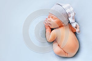 Newborn baby boy in the bonnet sleeping on the light blue background