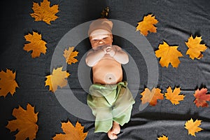 Newborn baby boy lies in autumn with maple leaves