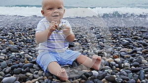 Newborn baby boy plays at the windy seaside with stones