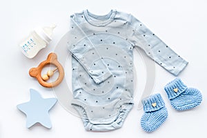 Newborn baby boy set - blue clothes as bodysuit, booties, toys - on white table top-down