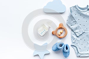 Newborn baby boy set - blue clothes as bodysuit, booties, toys - on white table top-down frame copy space