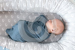 Newborn baby boy sleeping and swaddled in blue cloth lying in grey nest.