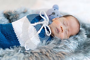 Newborn baby boy sleeping and swaddled in a knit wrap on bed