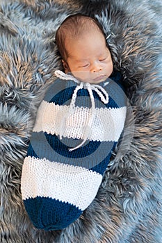 Newborn baby boy sleeping and swaddled in a knit wrap on bed
