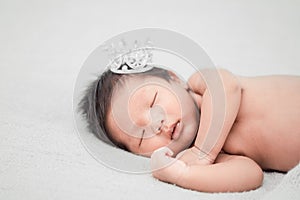 Newborn baby boy sleeping and wearing a silver crown.