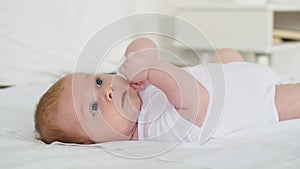 newborn baby boy smiling on a white bed at home, family with a small child, close-up, place for text, cute baby sucking