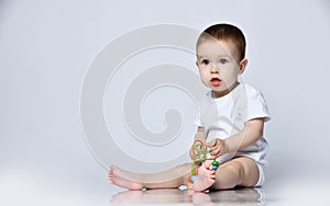 Newborn baby boy toddler is occupied playing with a multi-colored developing toy for kids sitting on the floor on a gray