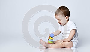 Newborn baby boy toddler playing with a multi-colored developing pyramid it on a gray with copy space