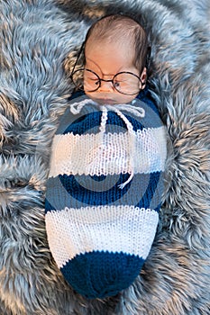 Newborn baby boy wearing glasses sleeping and swaddled in a knit wrap on bed