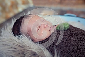 Newborn baby boy wrapped in brown wrap on furry blanket. Baby sleeping. Infant with long dark hair. The baby is holding a heart in