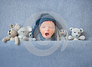 Newborn baby boy yawning and lying between plush toys