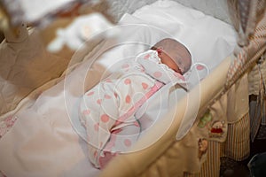A newborn baby in clothes lies in a cradle and sleeps sweetly